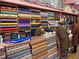 Fabric shop  Most of the fabric comes from India.  The fabric in front of the counter is destined for the traditional men's clothing, the gho.  The men in the image are wearing these.  The cloth behind the counter will be made into keras, the ankle length dresses worn by women.